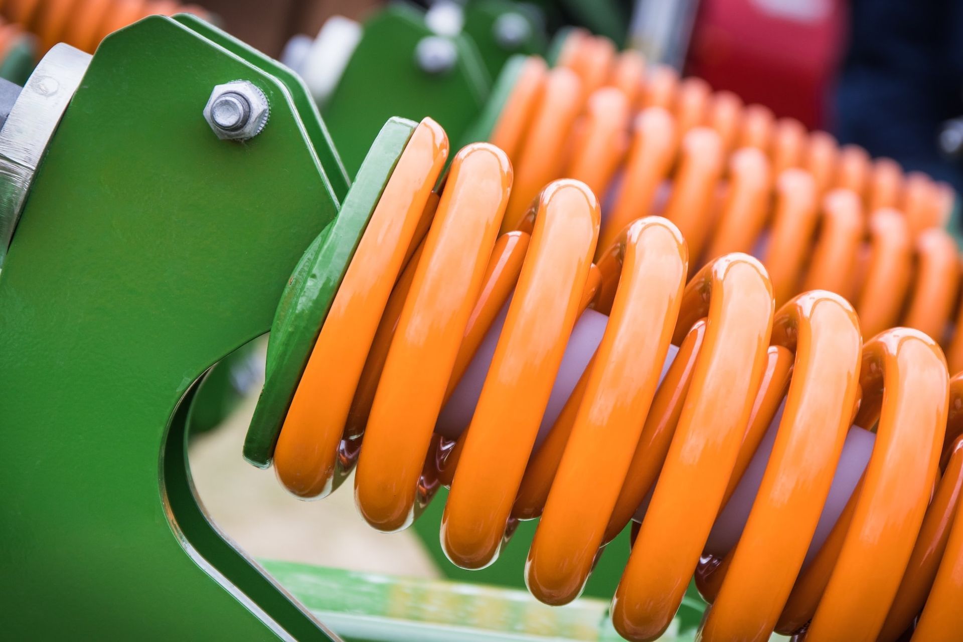 Leuchtend orangefarbene Schraubenfedern, die an grünen Metallmaschinenteilen befestigt sind.