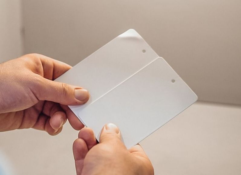 Hände halten zwei übereinanderliegende weiße Kunststoff-Testplatten mit kleinen Löchern in den Ecken.