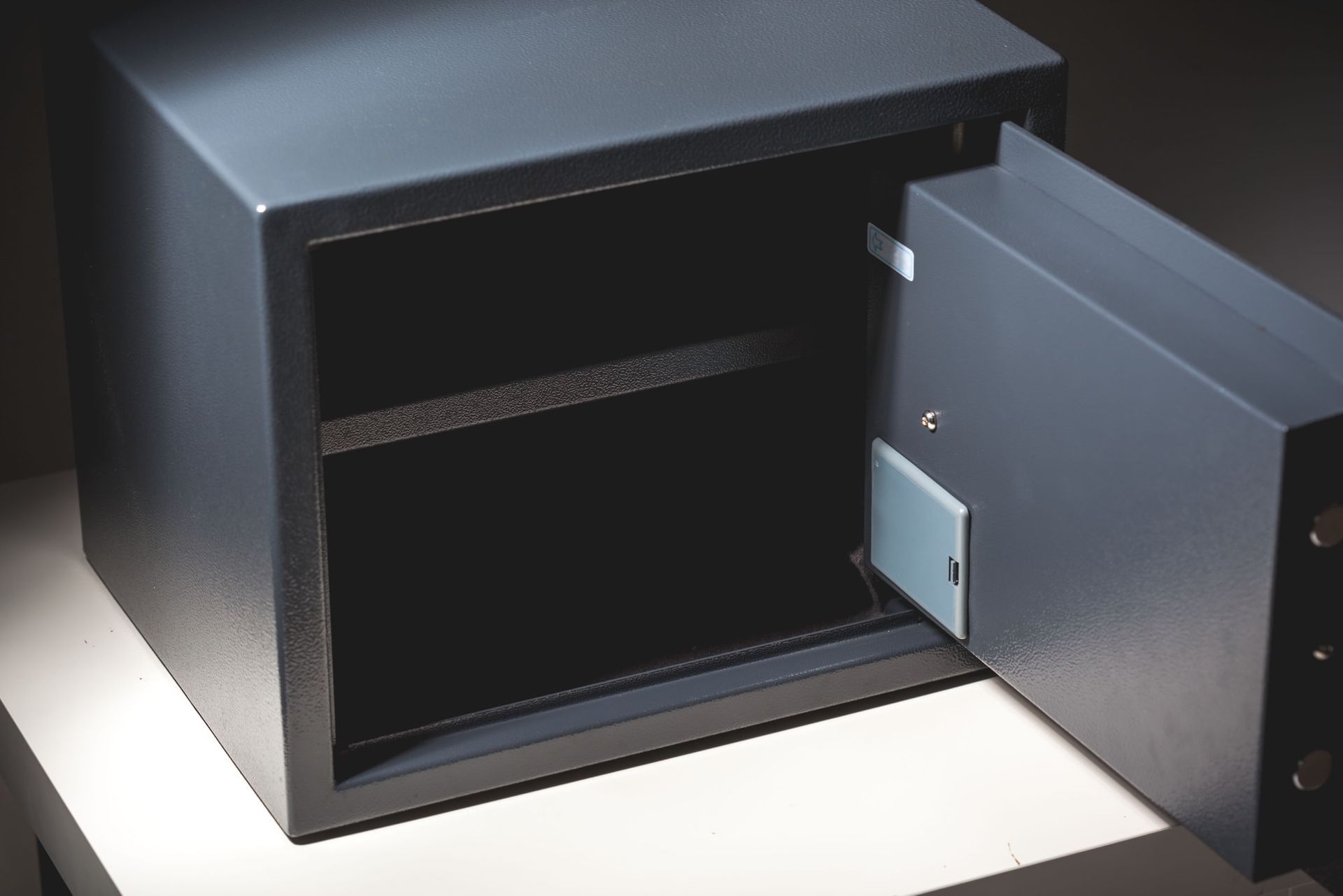 Ein offener, grauer Metalltresor steht auf einer weißen Fläche vor dunklem Hintergrund.