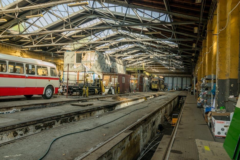 Old tram depot with a red-and-white tram, tracks, and maintenance equipment under a metal roof
