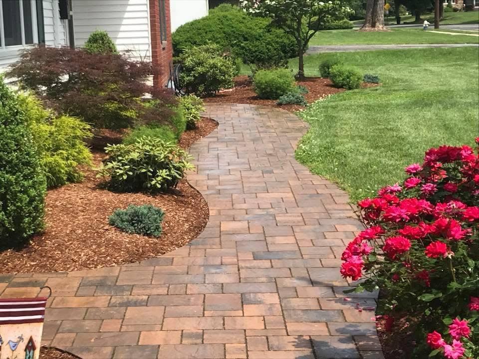 Manicured front yard with green lawn, mulch beds, and a curved border beside a house and sidewalk