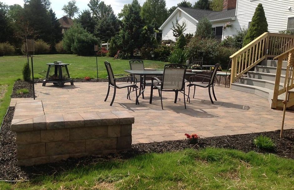 Curved stone patio with outdoor seating, lanterns, and lush landscaped garden under a cloudy sky