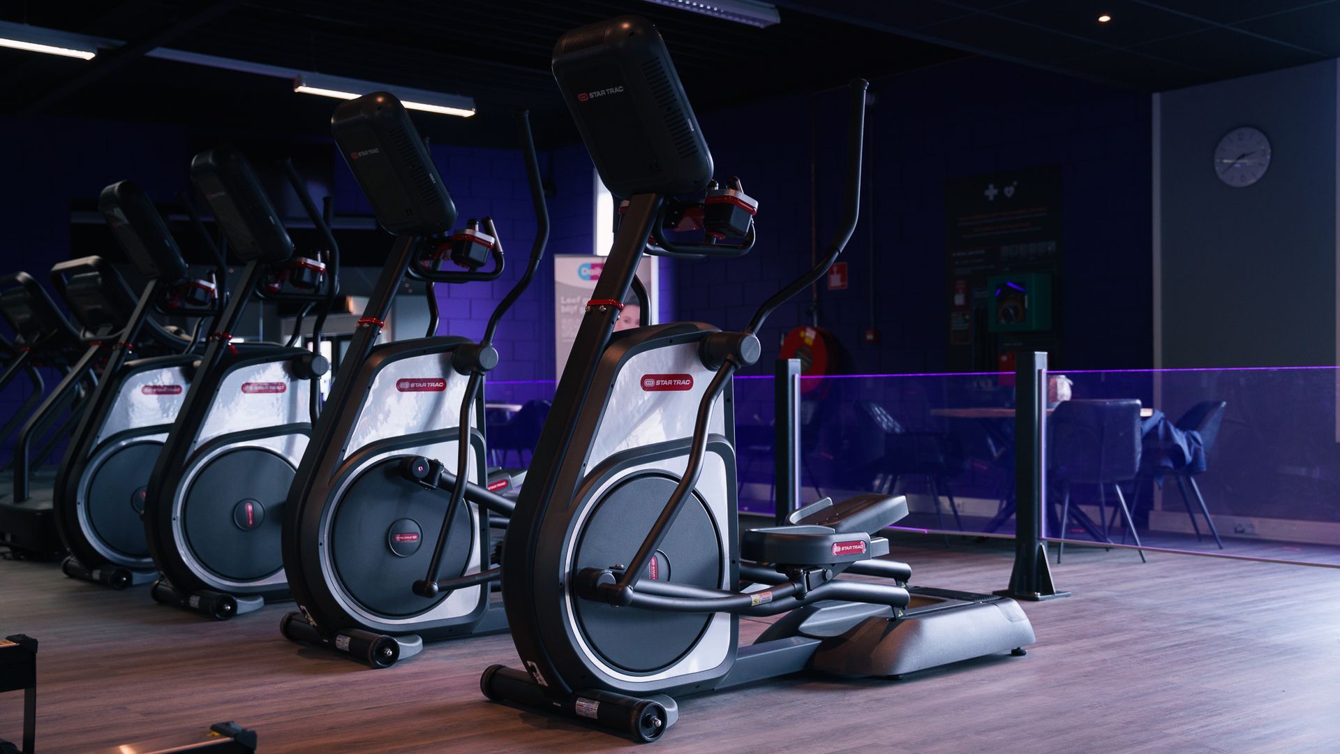 In een gymzaal staat een rij crosstrainers opgesteld.