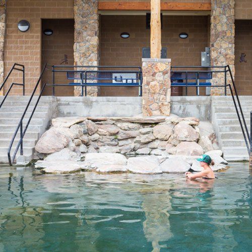 A person is swimming in a hot springs pool with stairs leading up to it.