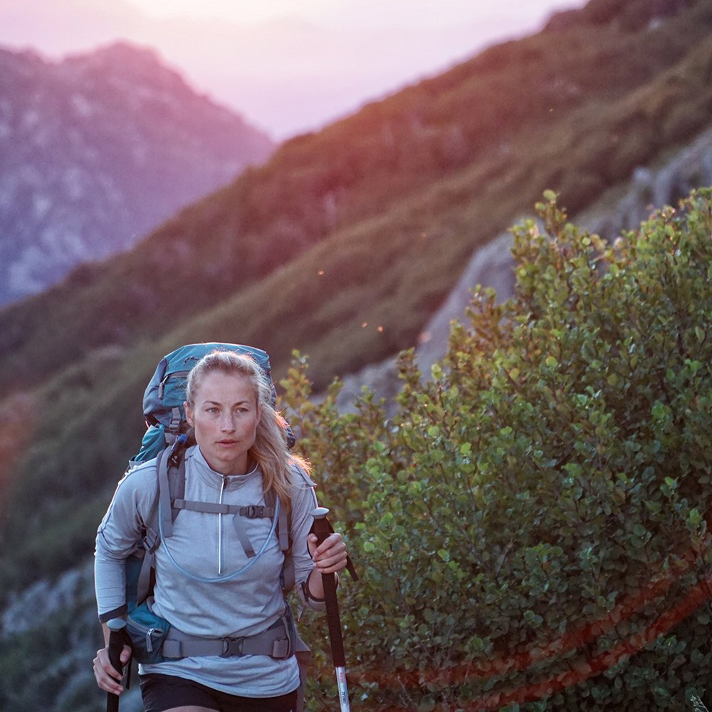 A woman with a backpack and hiking poles is walking up a hill.