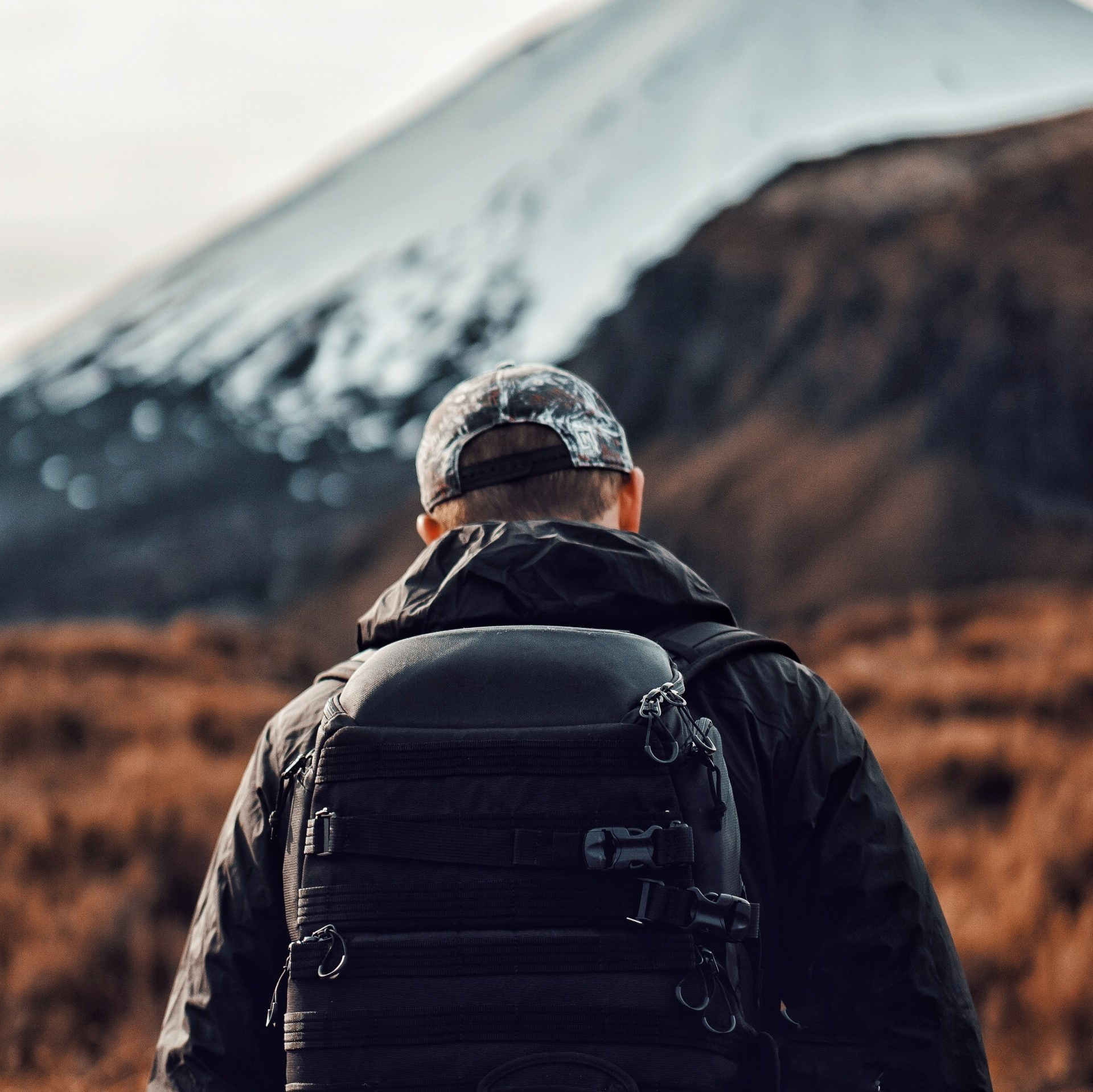 A man with a backpack is walking towards a mountain.