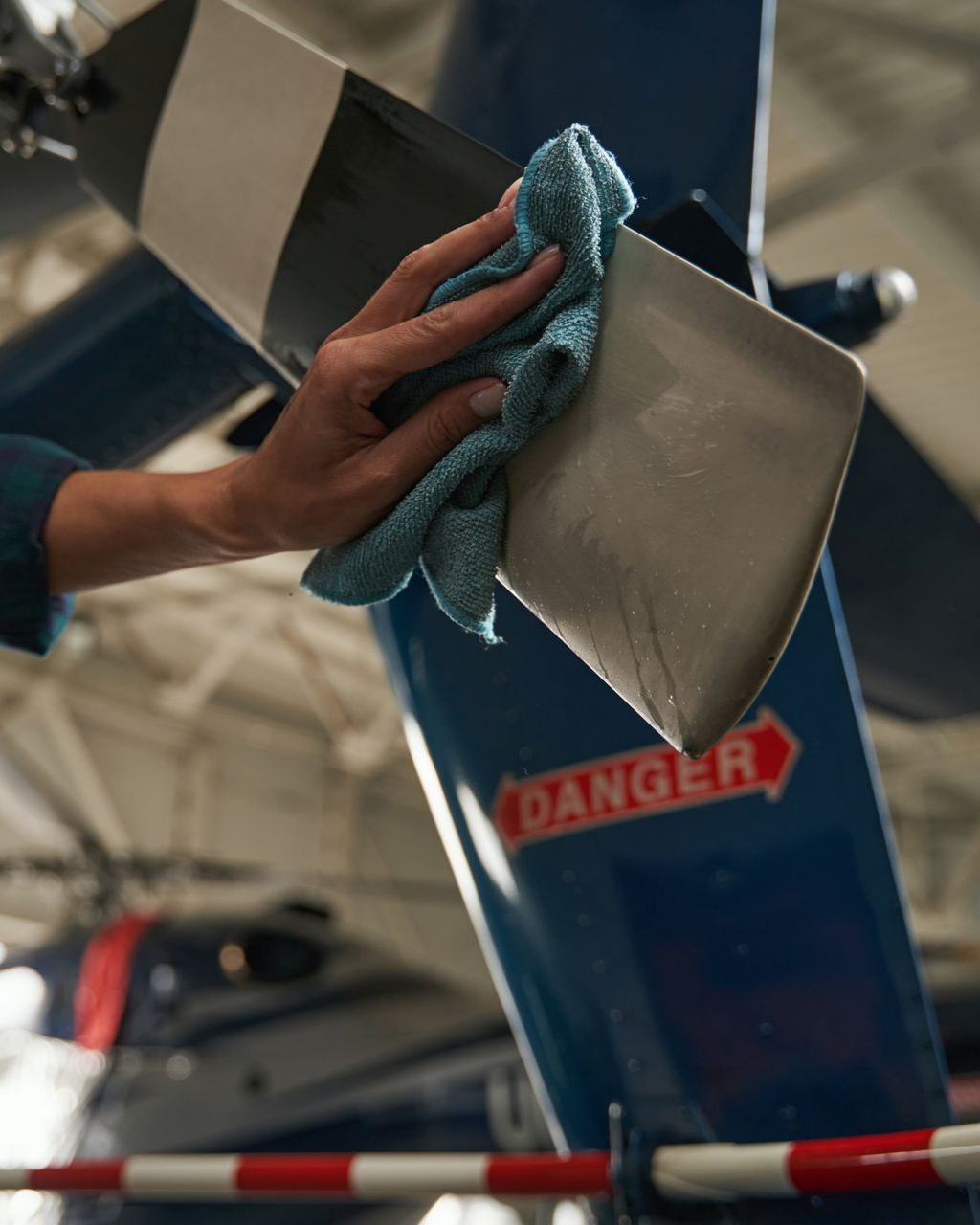 Person wiping down a helicopter rotor blade with a blue cloth, in a hangar.