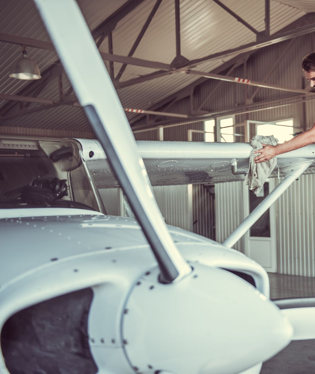 Man cleaning aircraft wing in a hangar, wearing blue overalls, using a cloth.