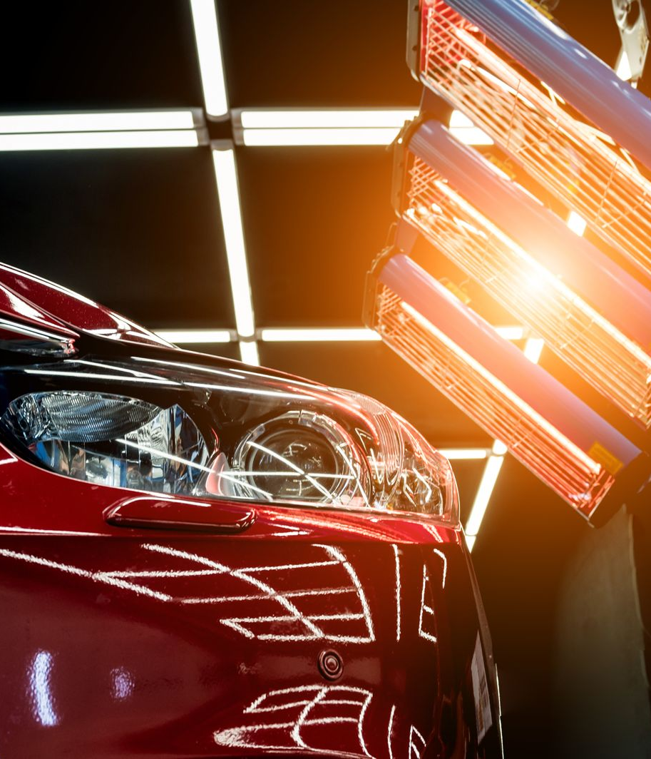 Red car under infrared paint drying lamps in a garage.