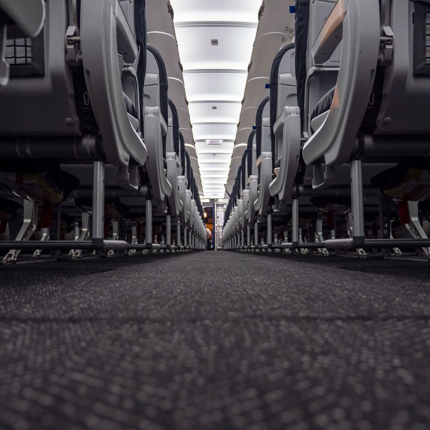 Airplane interior: rows of gray seats and carpeted aisle perspective.