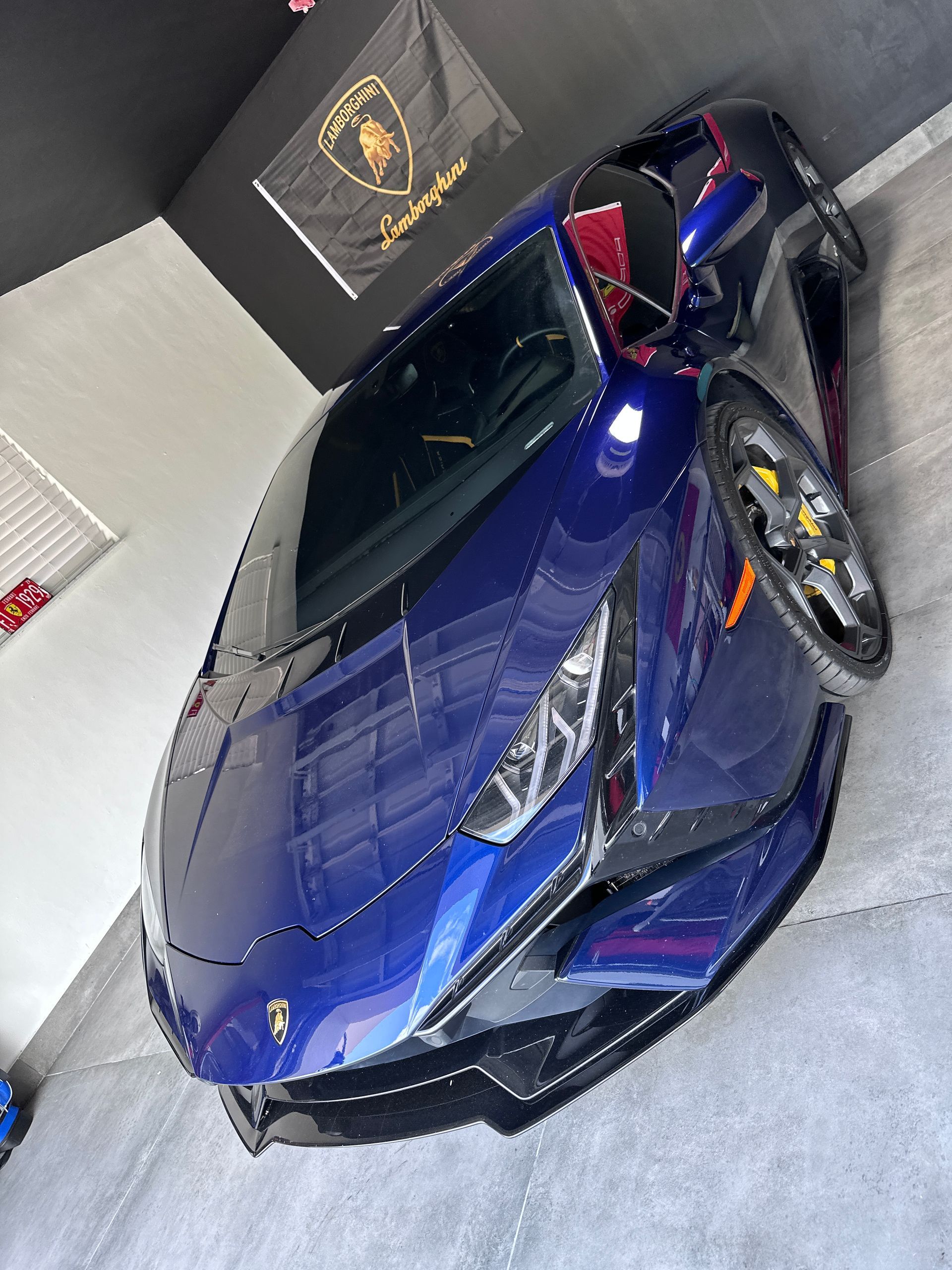 Green matte Tesla car parked on a road with black rims, palm trees, and a lake in the background.
