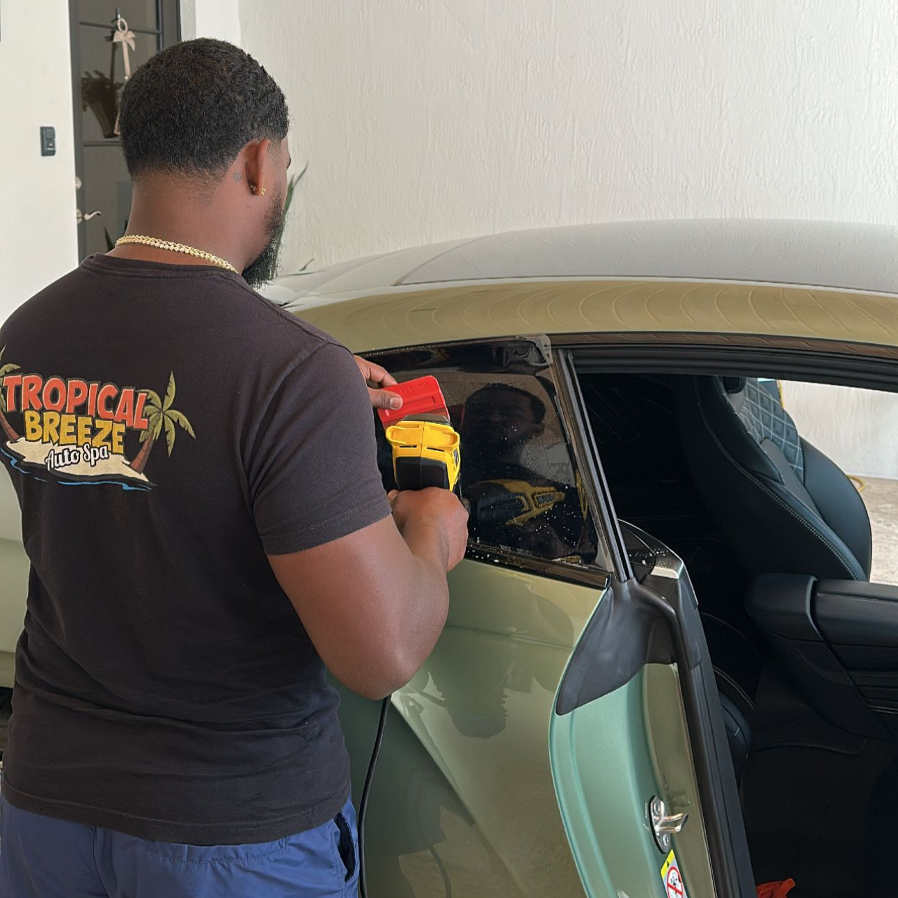 Person applying tint to a car window with a yellow and red squeegee; in a garage.