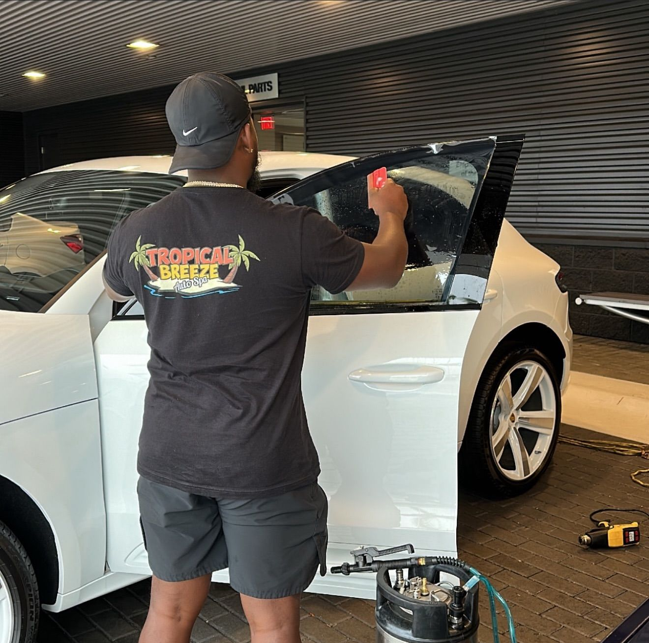 Person applying tint to a white car window inside a building.