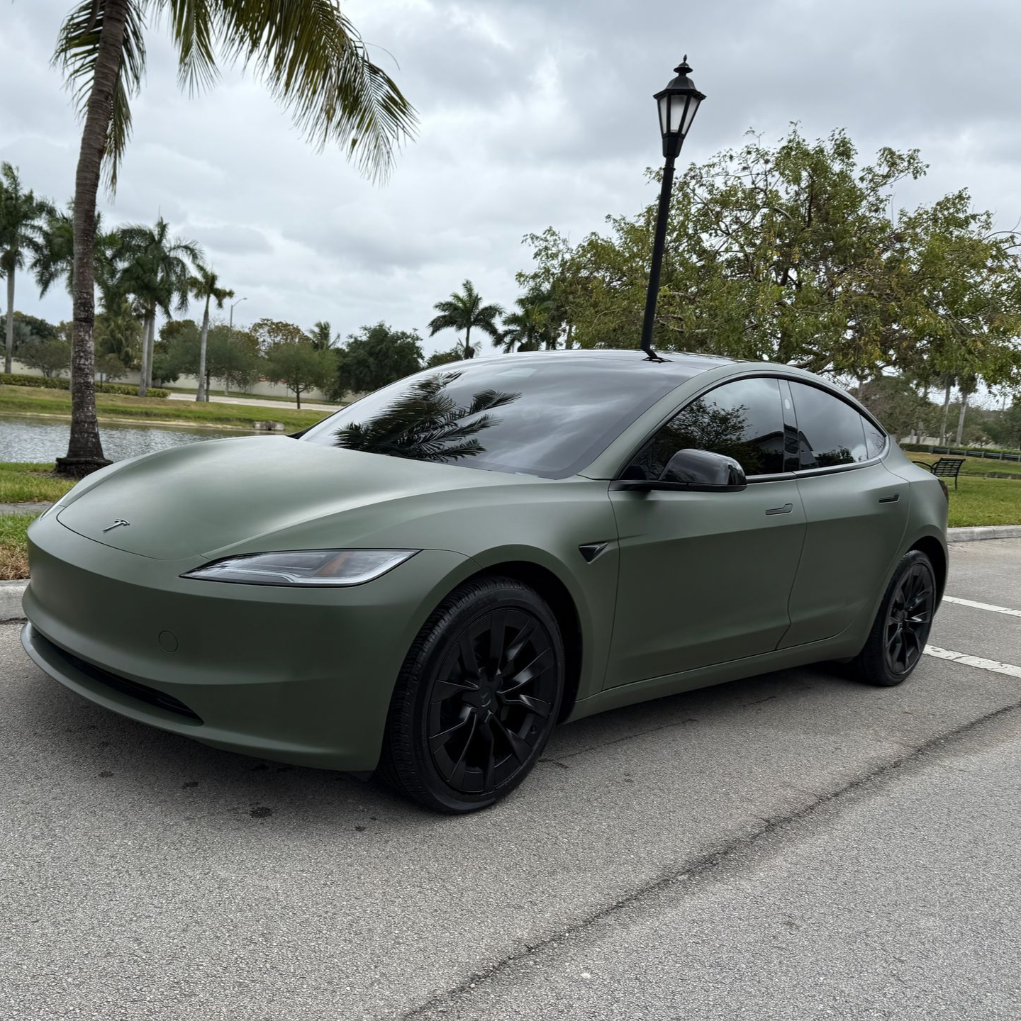 Hands applying window tint to a car window; green car in an indoor setting.