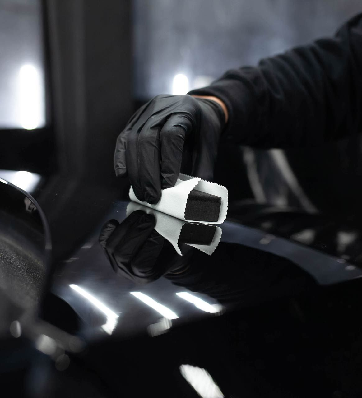 Gloved hand applying ceramic coating with applicator on black car surface.