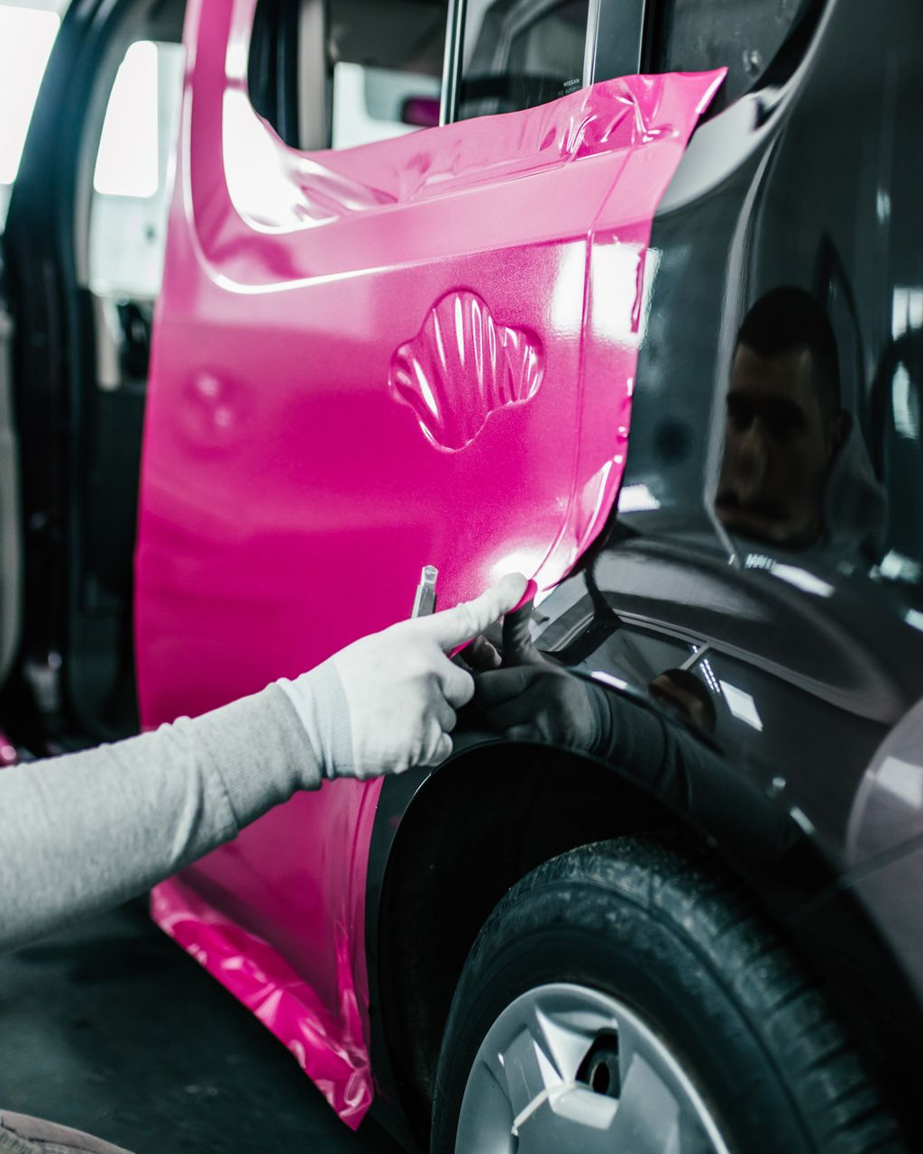 Car door being wrapped in pink vinyl by a gloved hand.