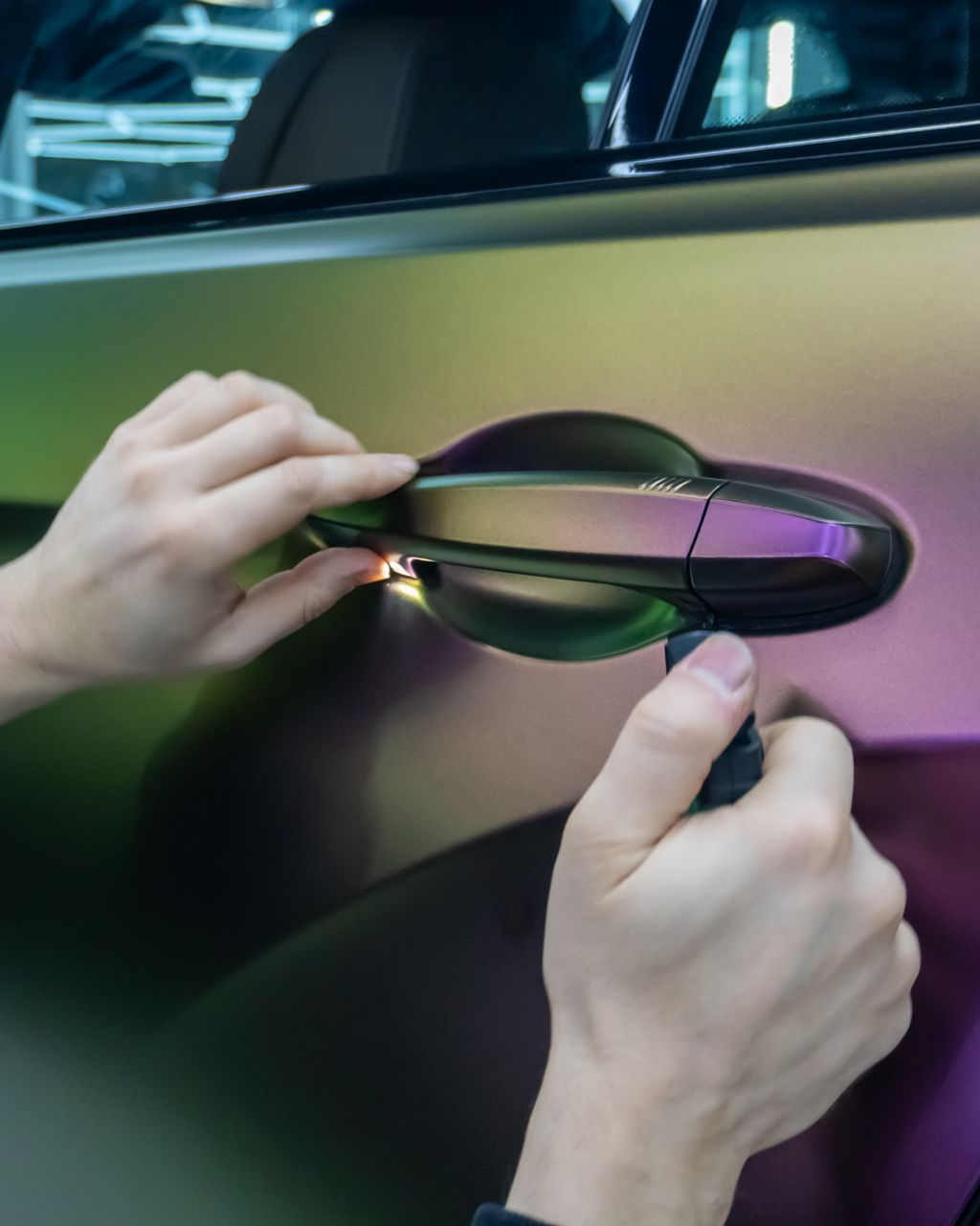 Hands installing iridescent wrap on a car door handle.