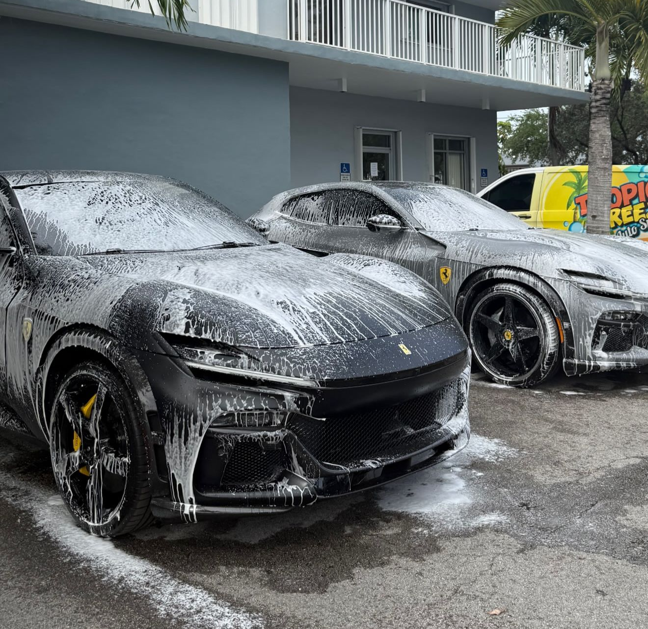 Two black Ferrari SUVs covered in soap suds, outside a building.
