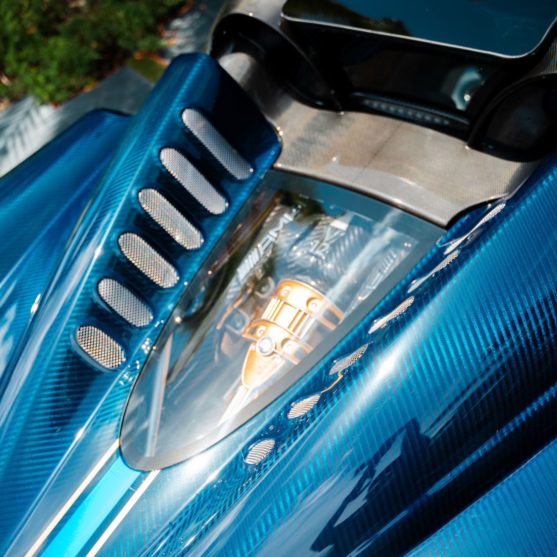Blue carbon fiber car hood with air vents and a clear window showing an engine component.