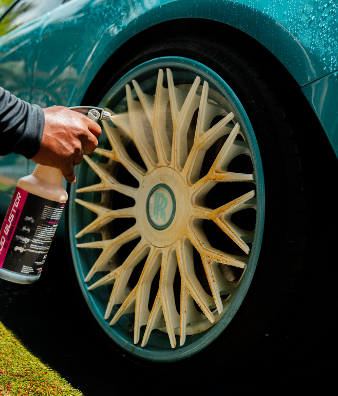 Person spraying cleaning solution on a dirty teal car wheel with a Rolls-Royce logo.