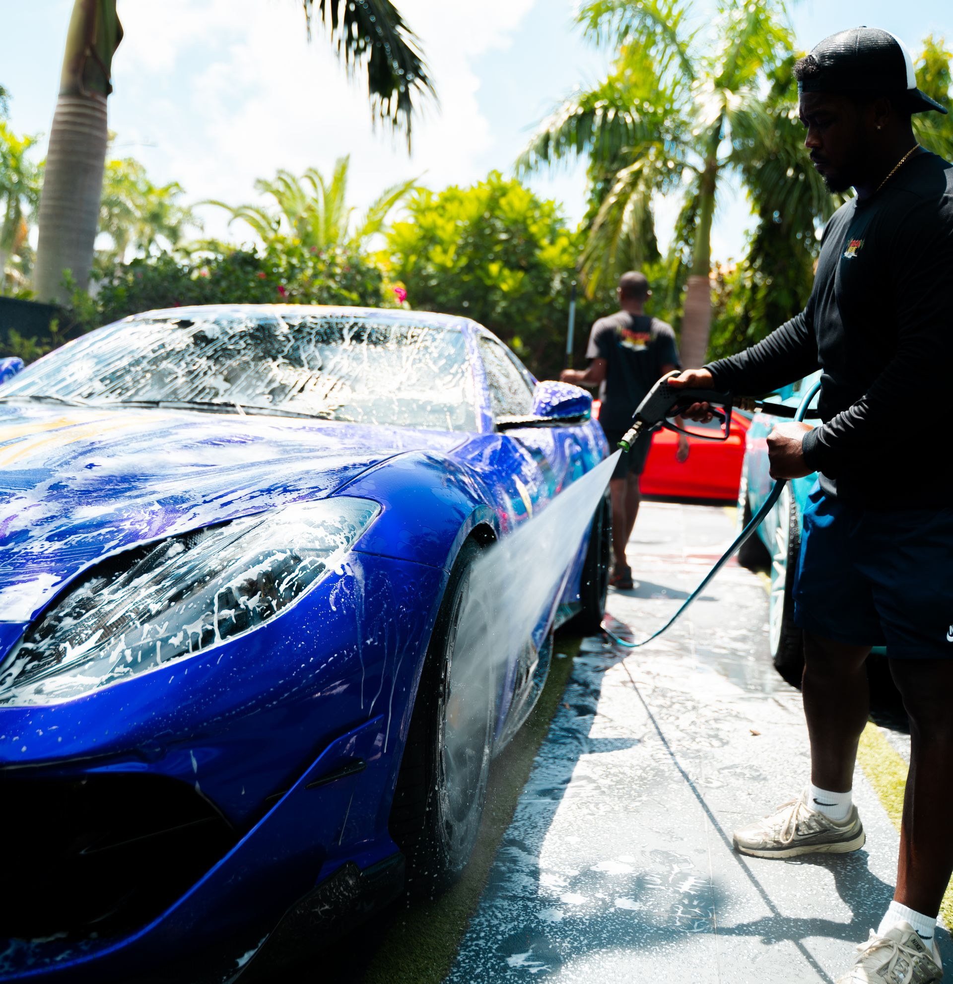 Man washing a blue sports car with a hose; outdoors.