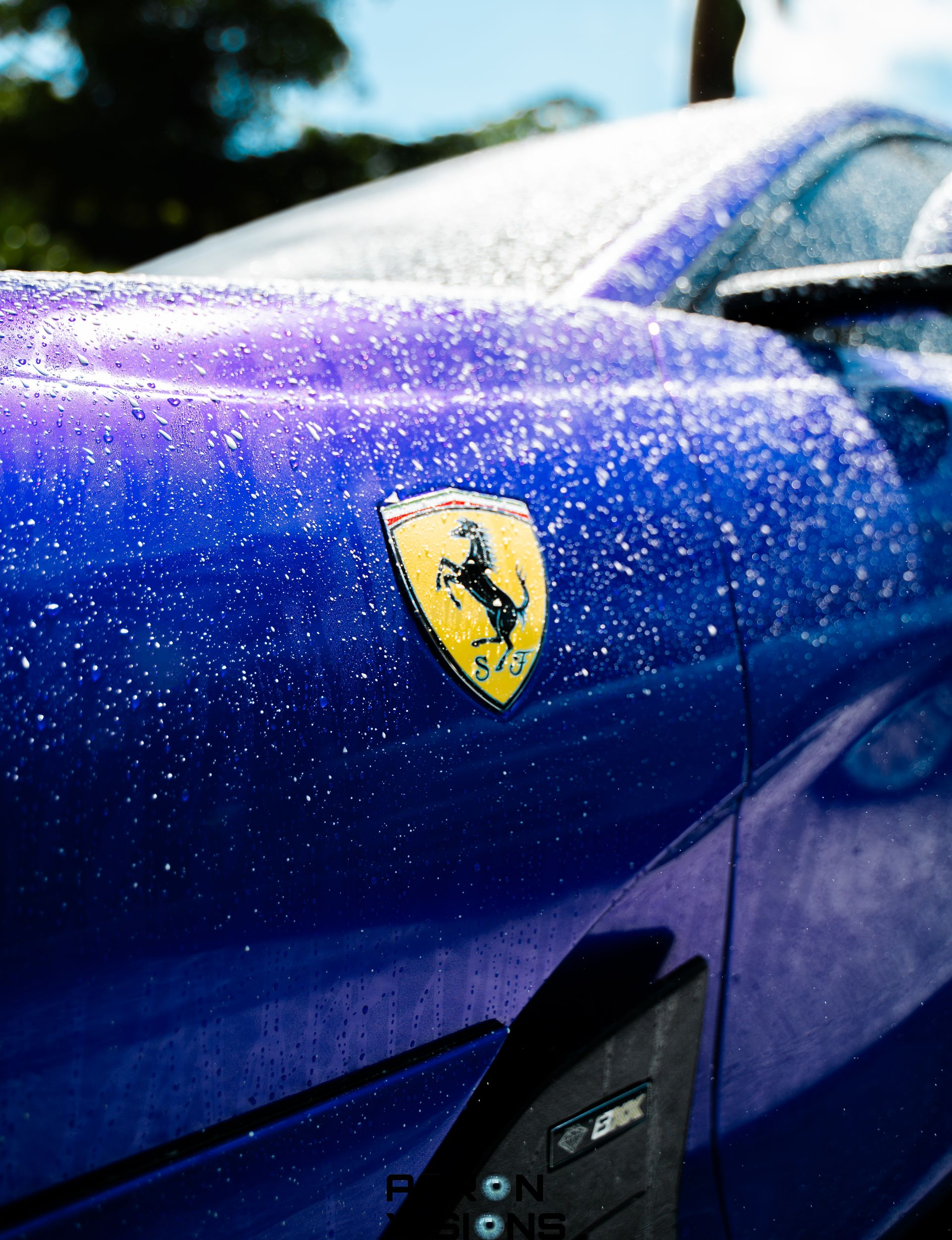 Blue Ferrari car with water droplets on the hood; Ferrari emblem visible.