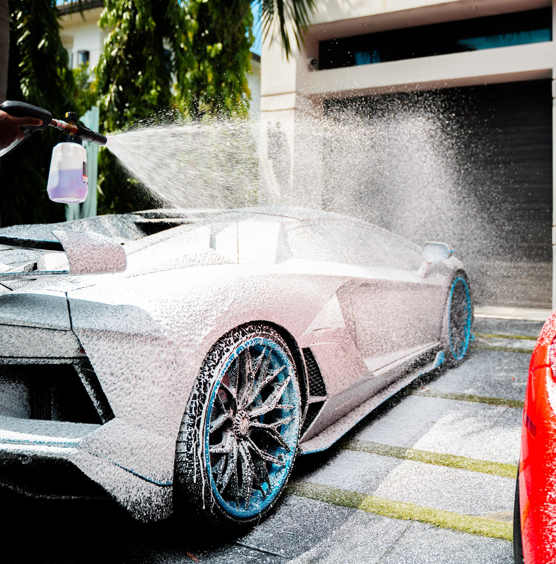 White sports car covered in foam being washed outside a garage.