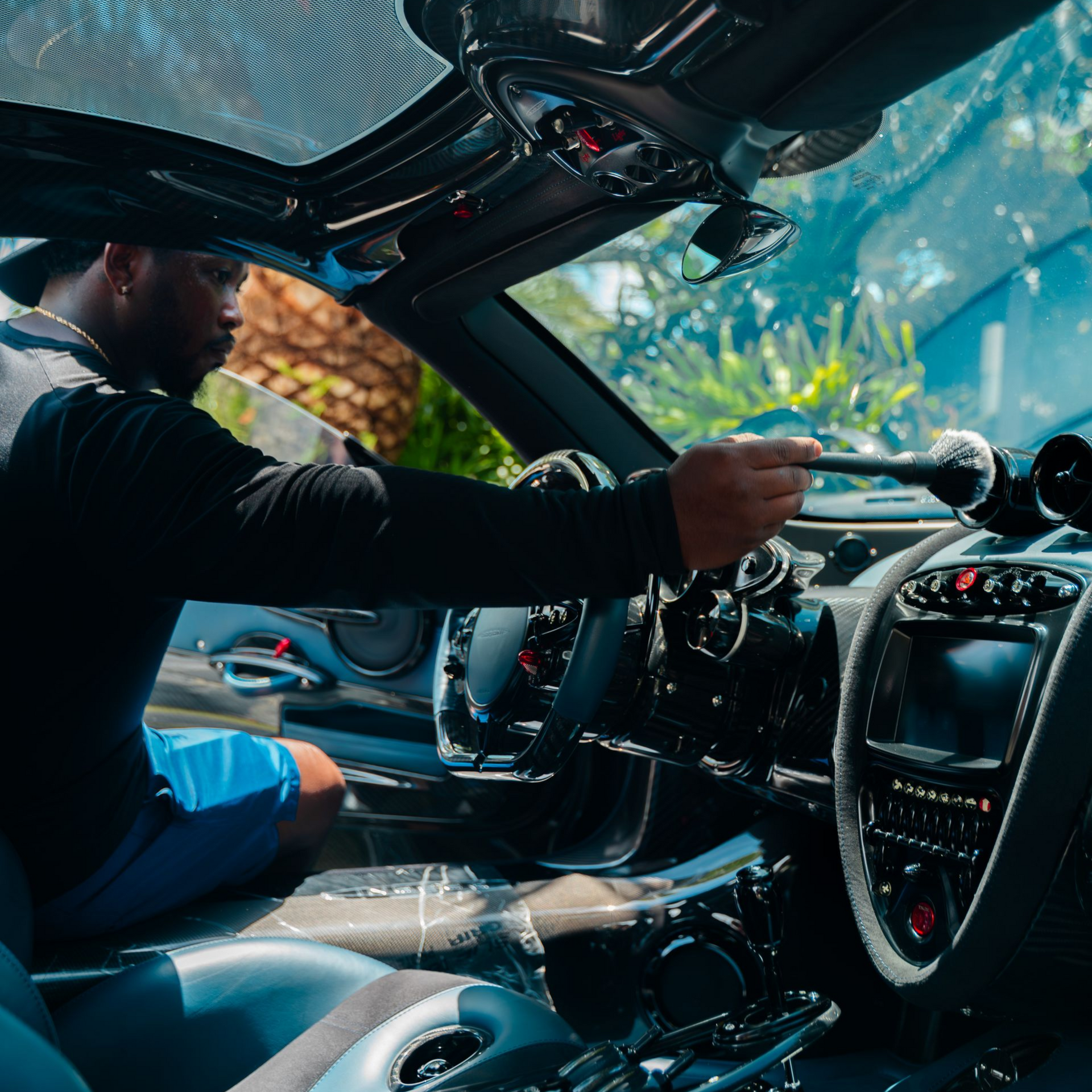 Person inside a luxury car, reaching toward the dashboard. The interior is dark with chrome accents.