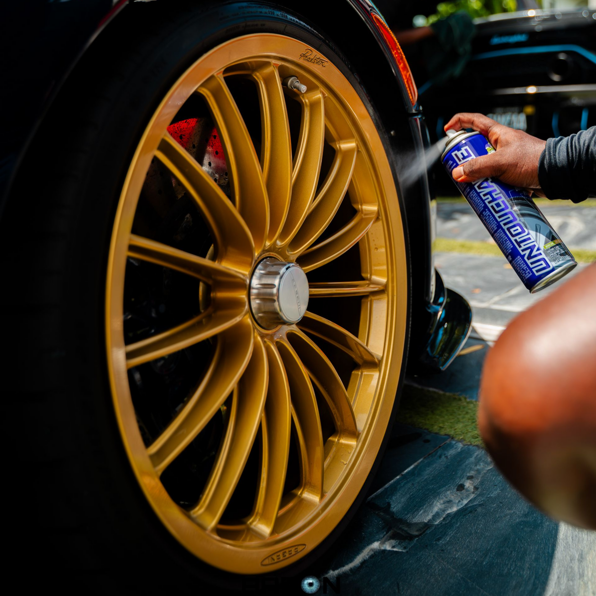 A person spraying gold car wheel with a cleaning product, outdoors.