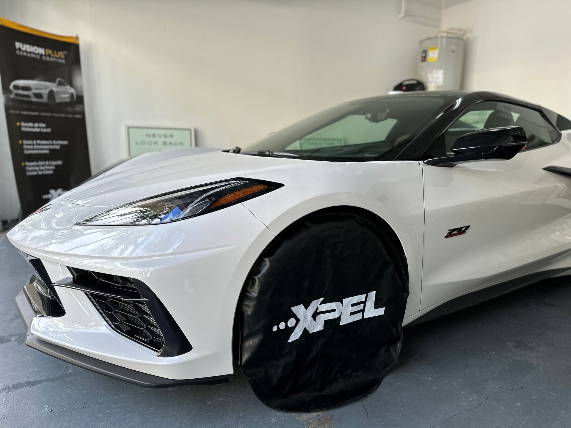 White Corvette with black accents, covered tire, parked indoors near a banner.