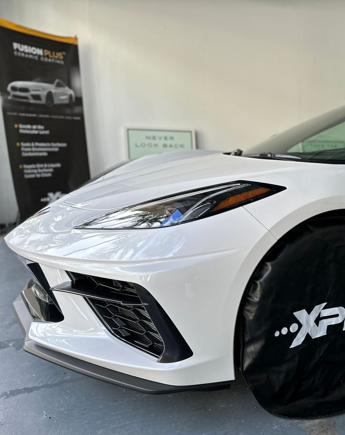 White sports car's front with a black wheel cover, parked near a Fusion Plus banner.