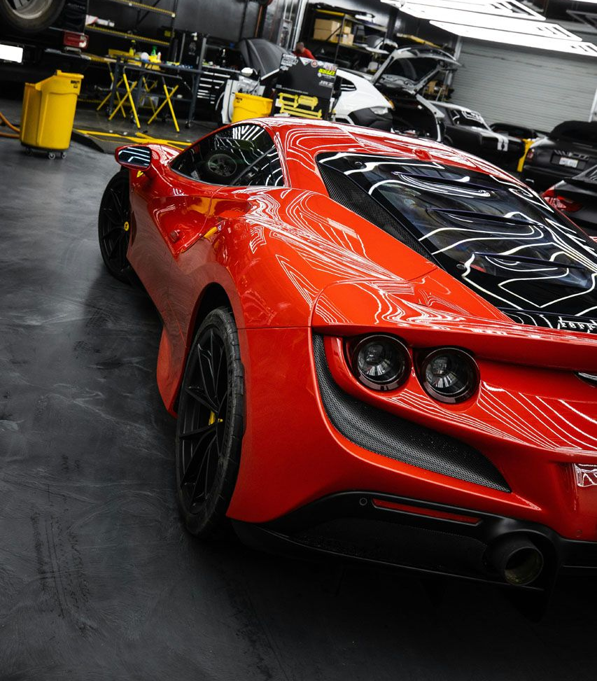 Red Ferrari sports car parked in a garage; dark interior, black wheels, exhaust pipes visible.
