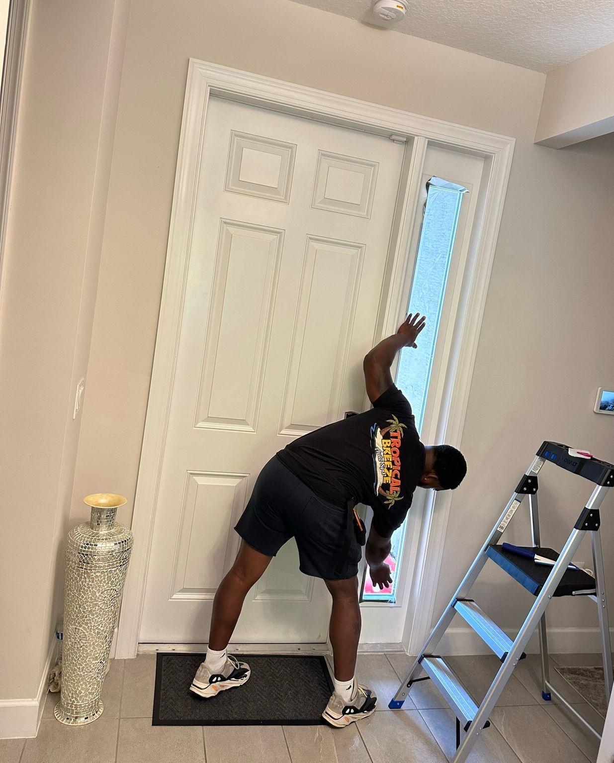 Man leaning into door, reaching towards window pane. Standing inside a house, near a small step ladder.