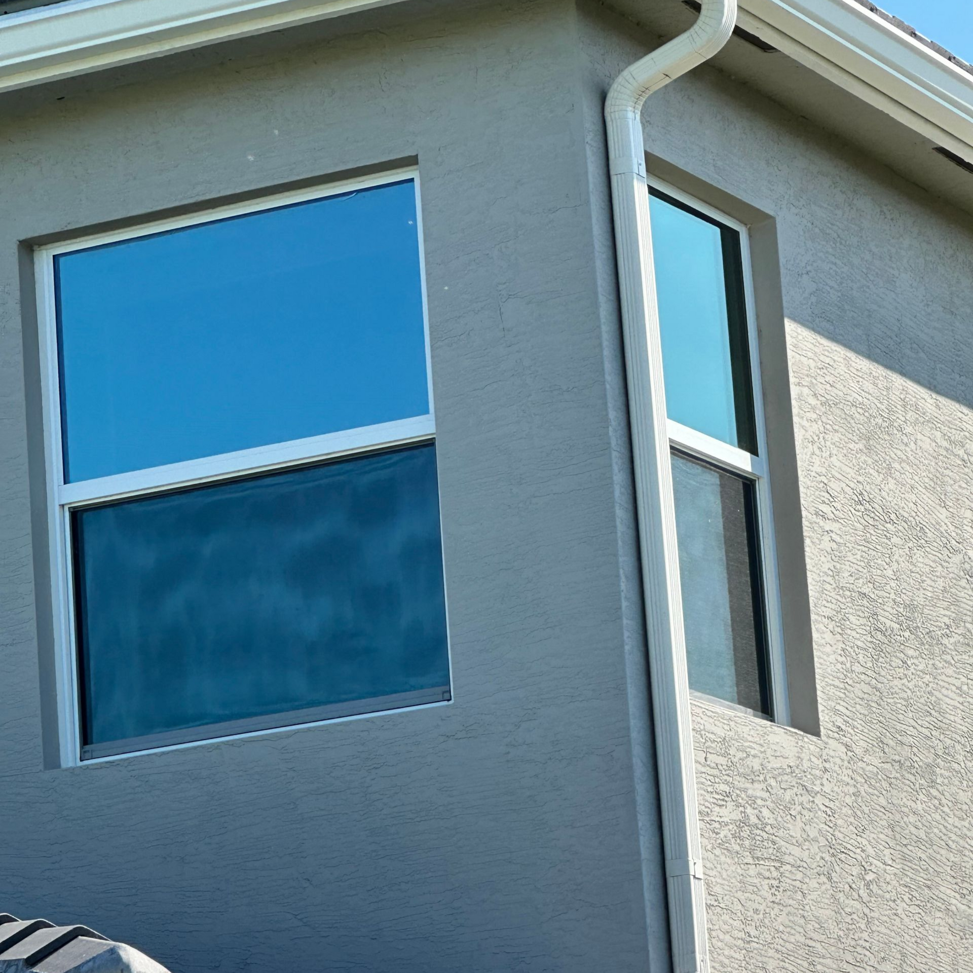 Two windows on a light gray stucco wall. One is rectangular, the other tall and narrow; both reflect blue sky.