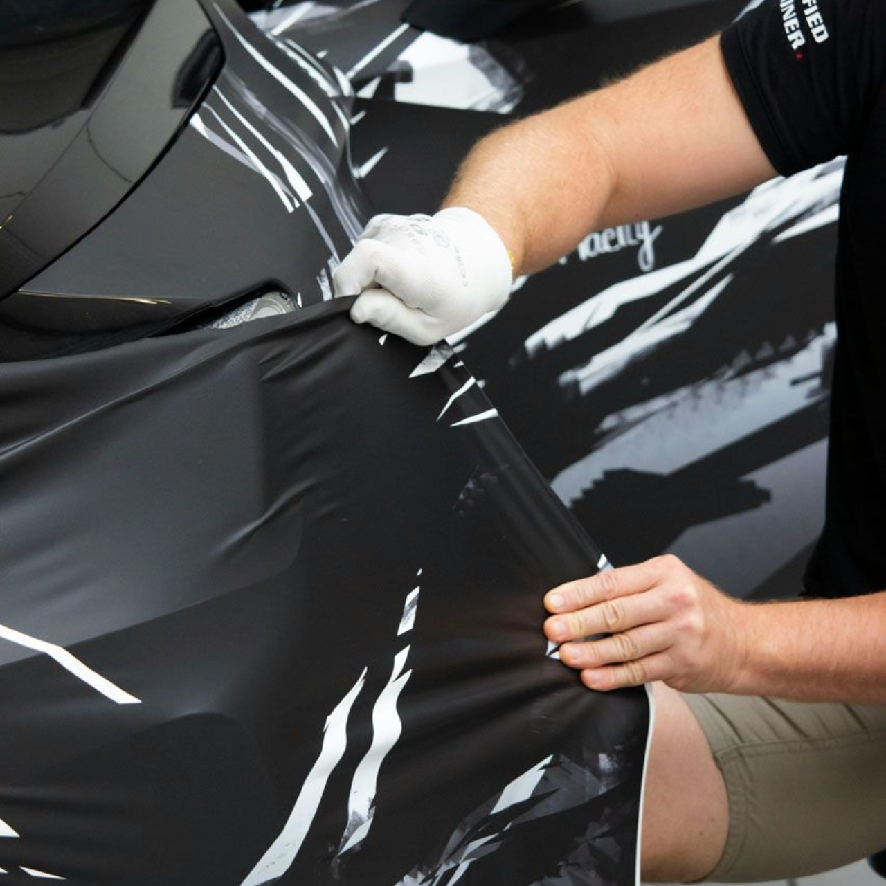Person wearing white gloves installing black car wrap on vehicle.