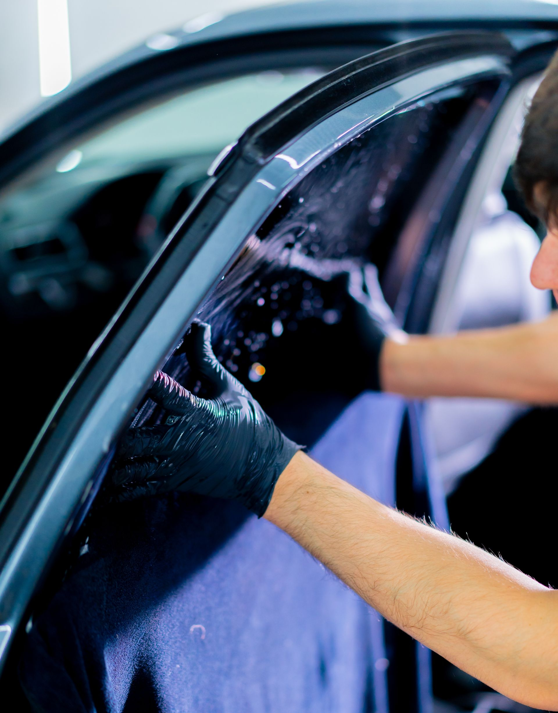 Person applying tint film to a car window, wearing black gloves.