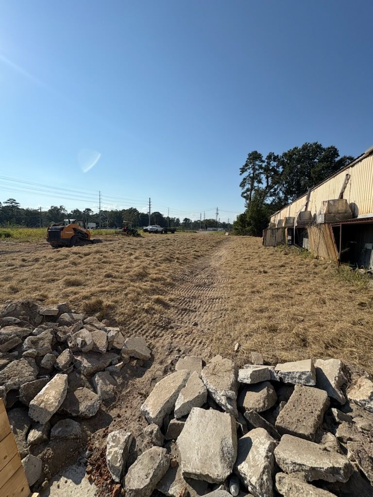 Demolished building site with debris in the foreground, tractor in the distance under a clear blue sky.