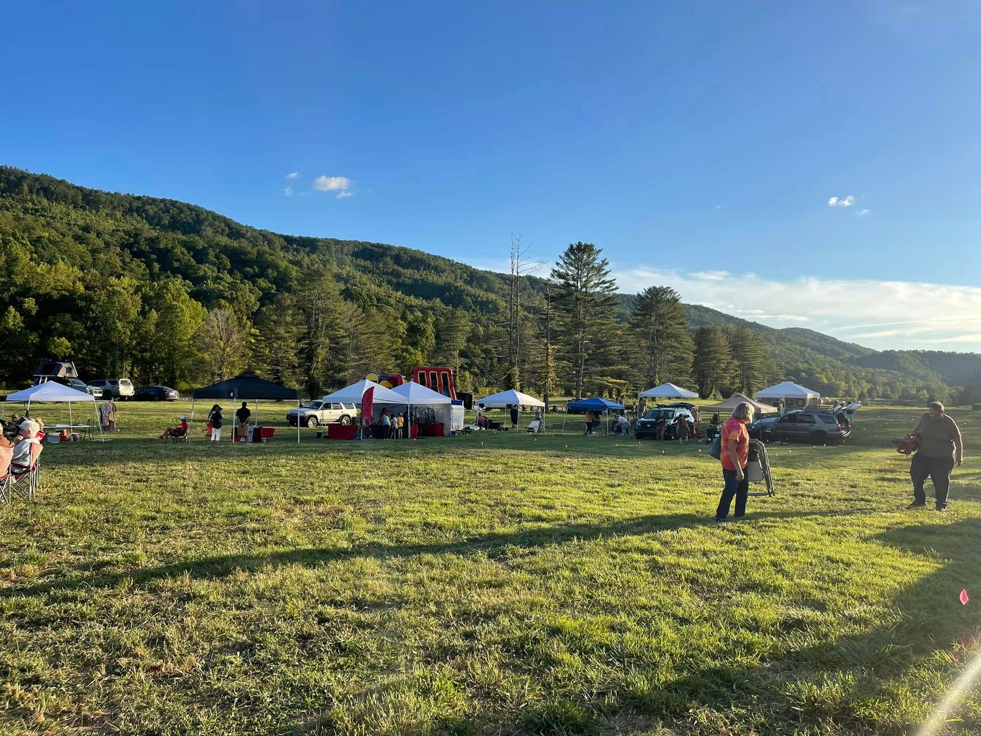 A group of people are standing in a grassy field with tents in the background.