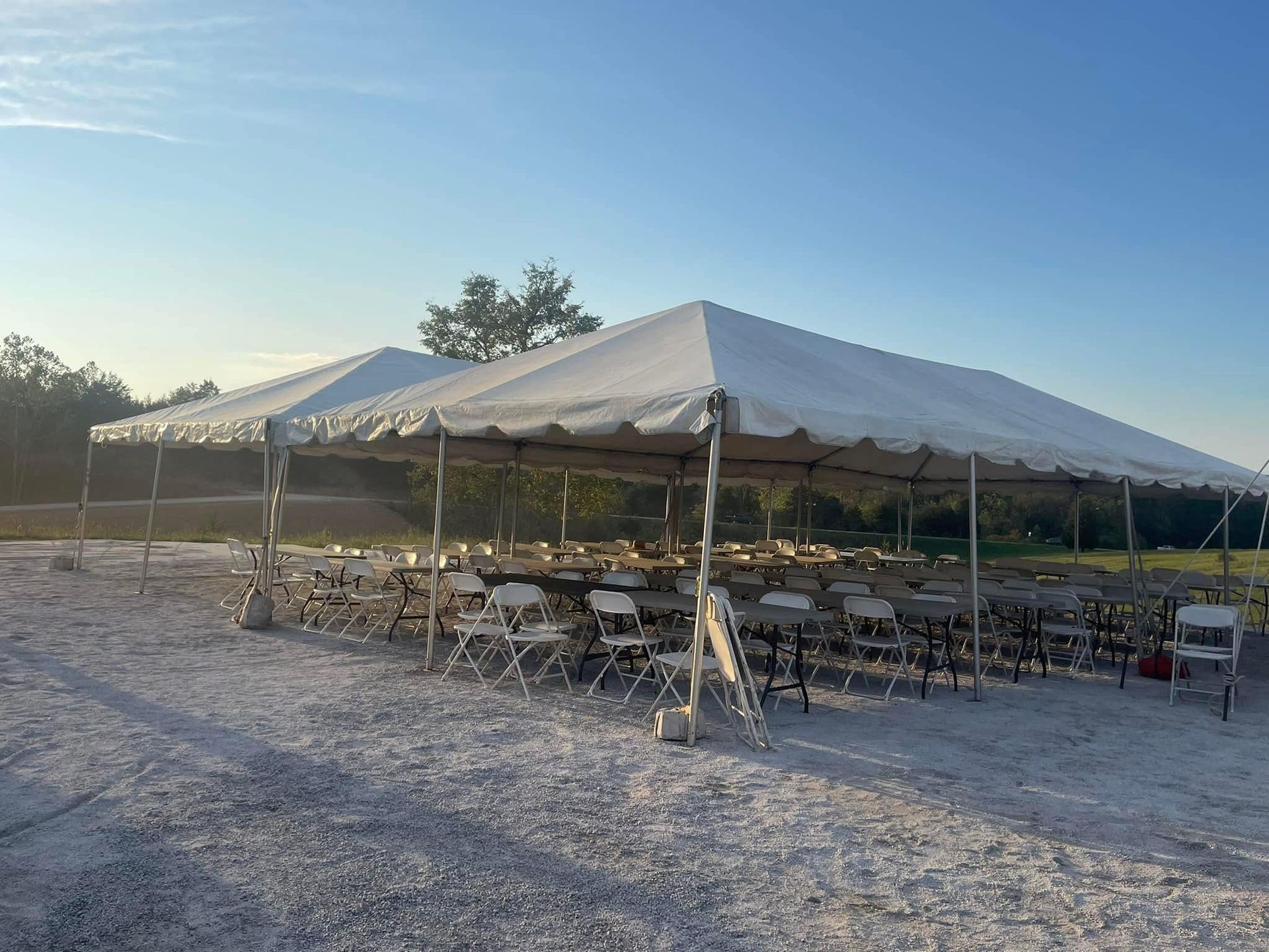 A large white tent with tables and chairs underneath it in a dirt field.
