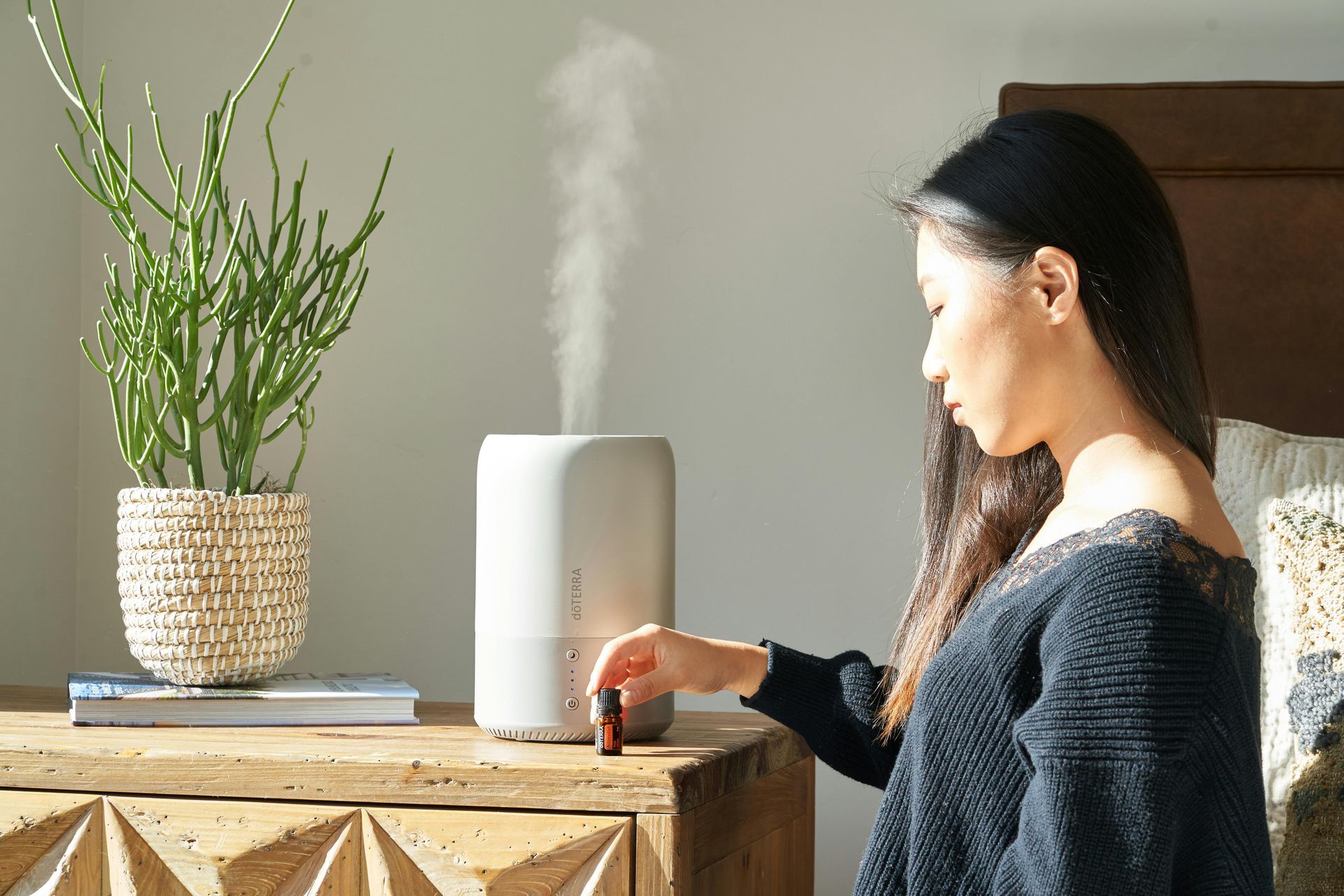 A woman is sitting on a nightstand using an essential oil diffuser.