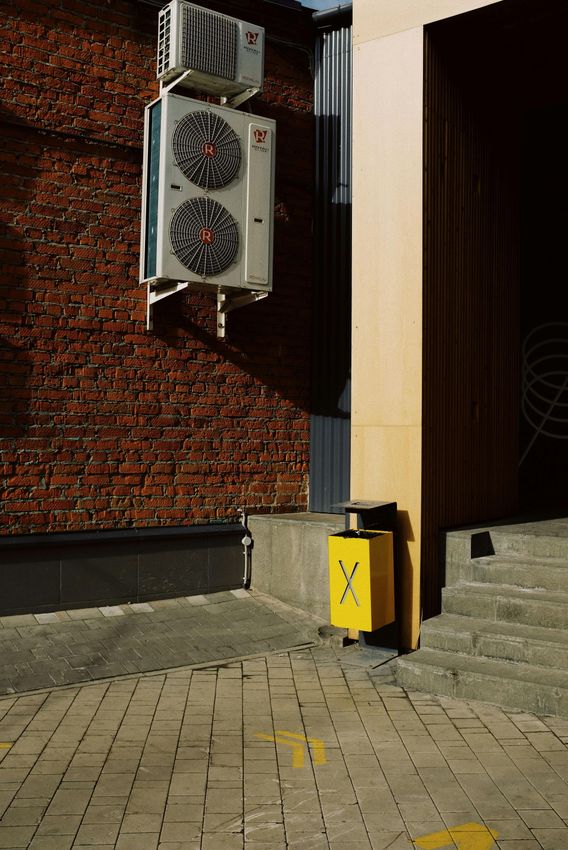 A yellow trash can is sitting on the sidewalk next to a brick wall.