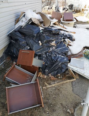 Storm-damaged yard cluttered with broken furniture, black tarp, and scattered debris beside a house