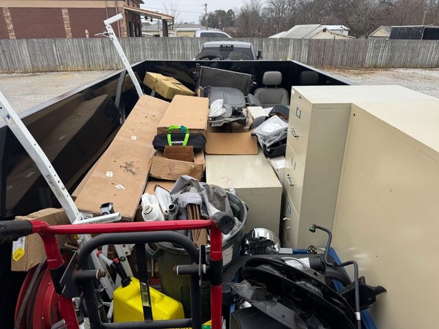 Truck bed filled with assorted household debris and furniture, parked outdoors in a snowy lot.