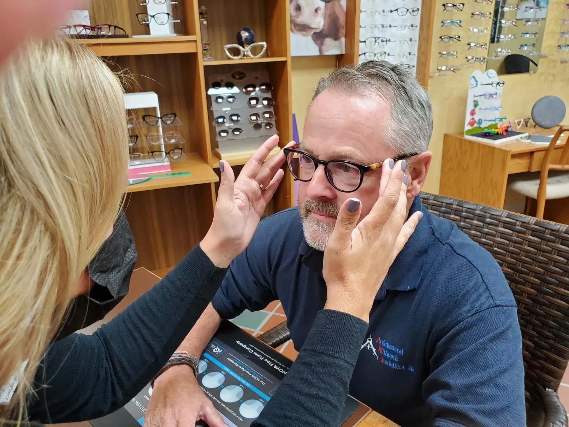 A person wearing glasses has them adjusted by another person in an eyewear shop.