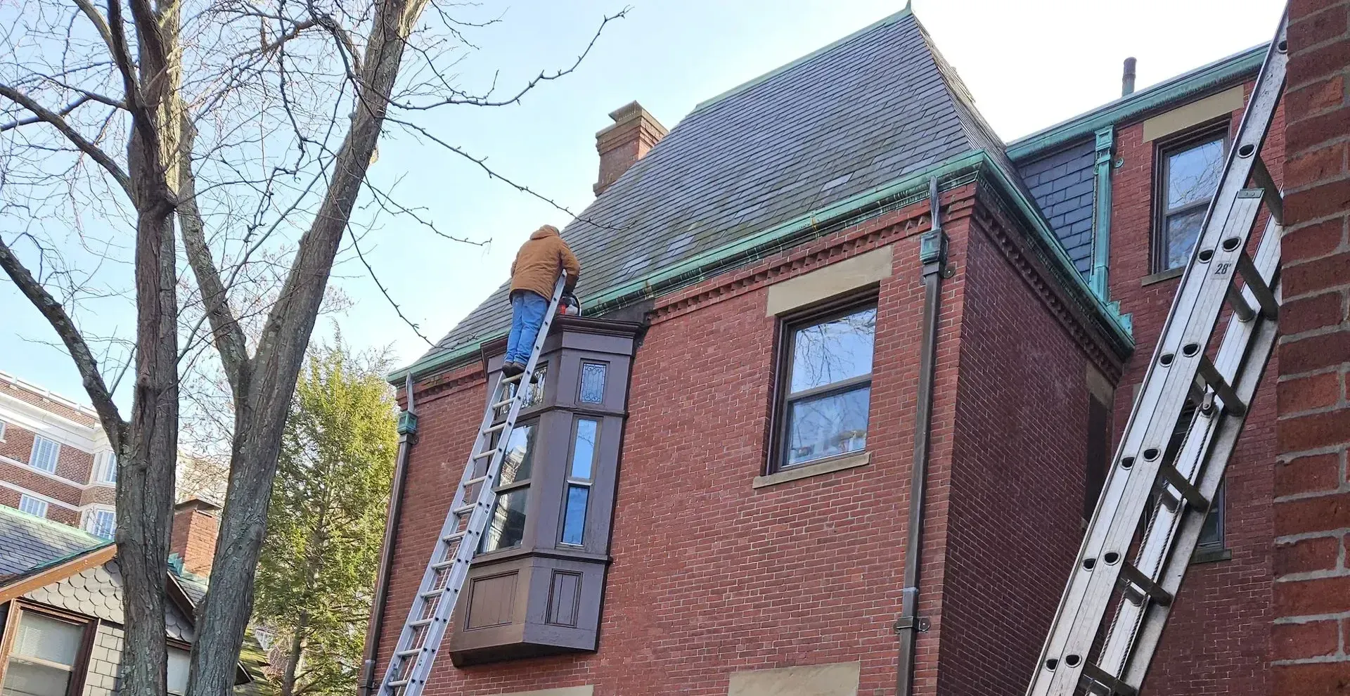 A man is standing on a ladder on the side of a brick building.