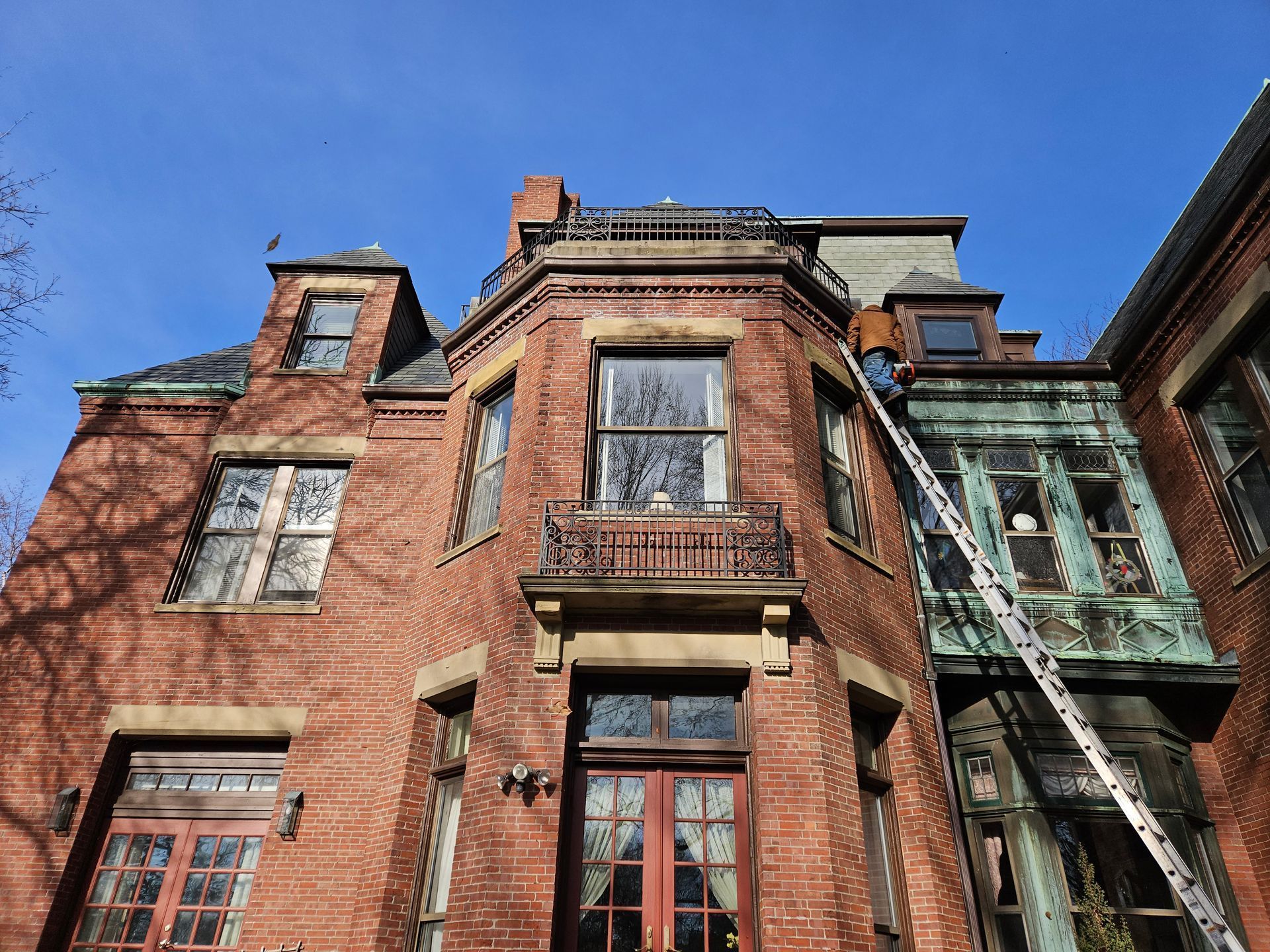 A man is standing on a ladder on the side of a brick building.