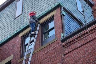 A man is standing on a ladder on the side of a brick building.