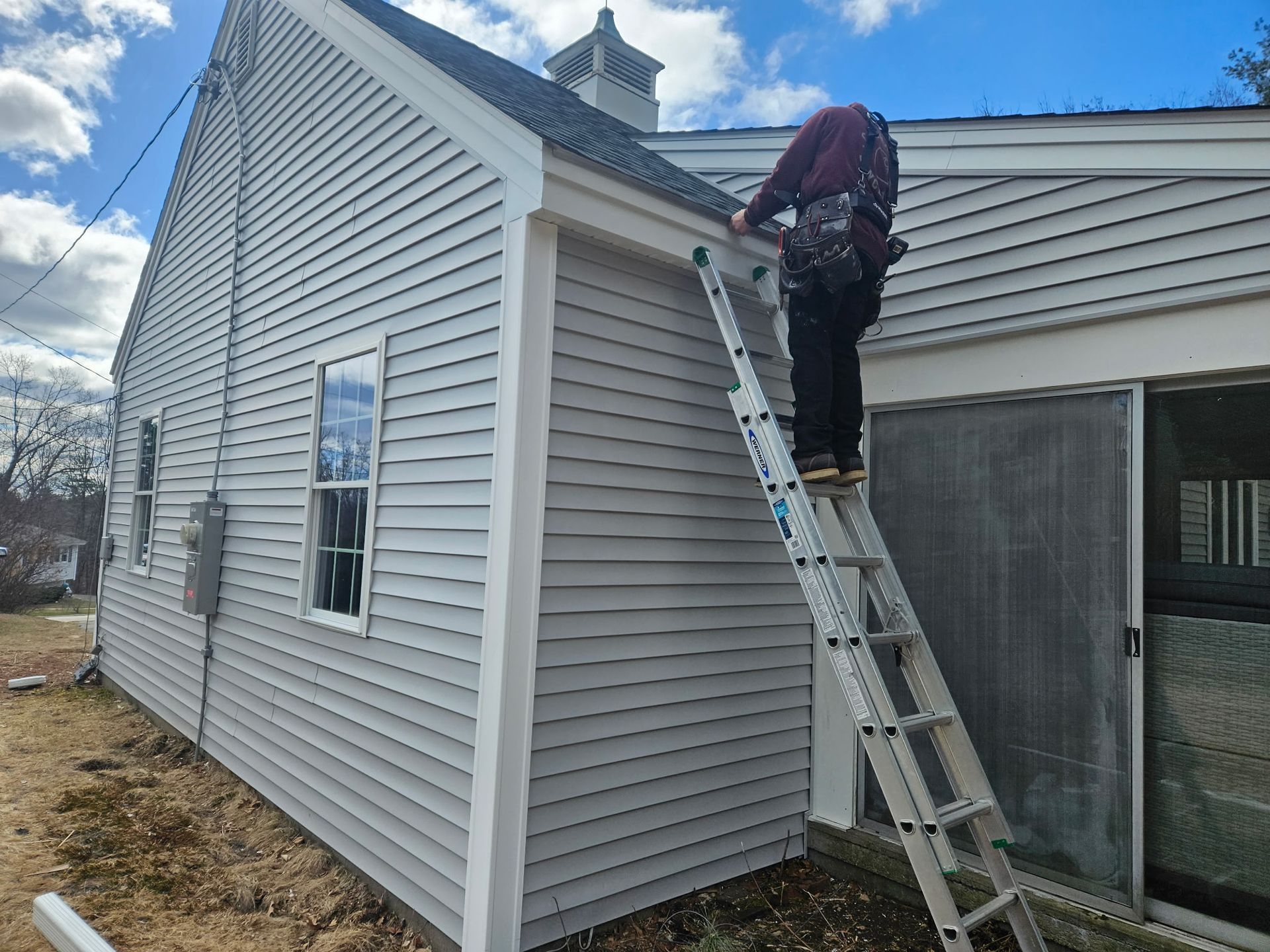 A man is standing on a ladder on the side of a brick building.