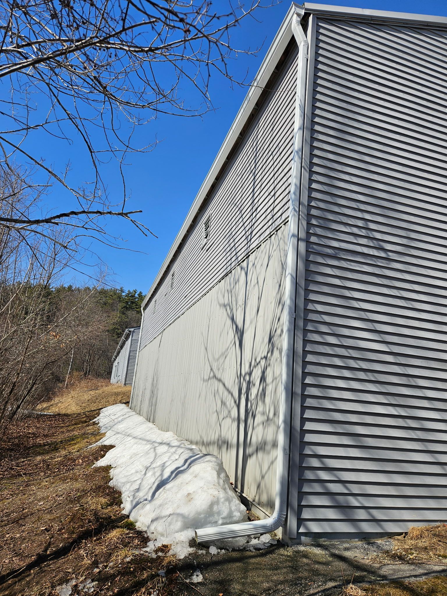 Gray building with horizontal siding and concrete base. Snow pile at base, sunny day.