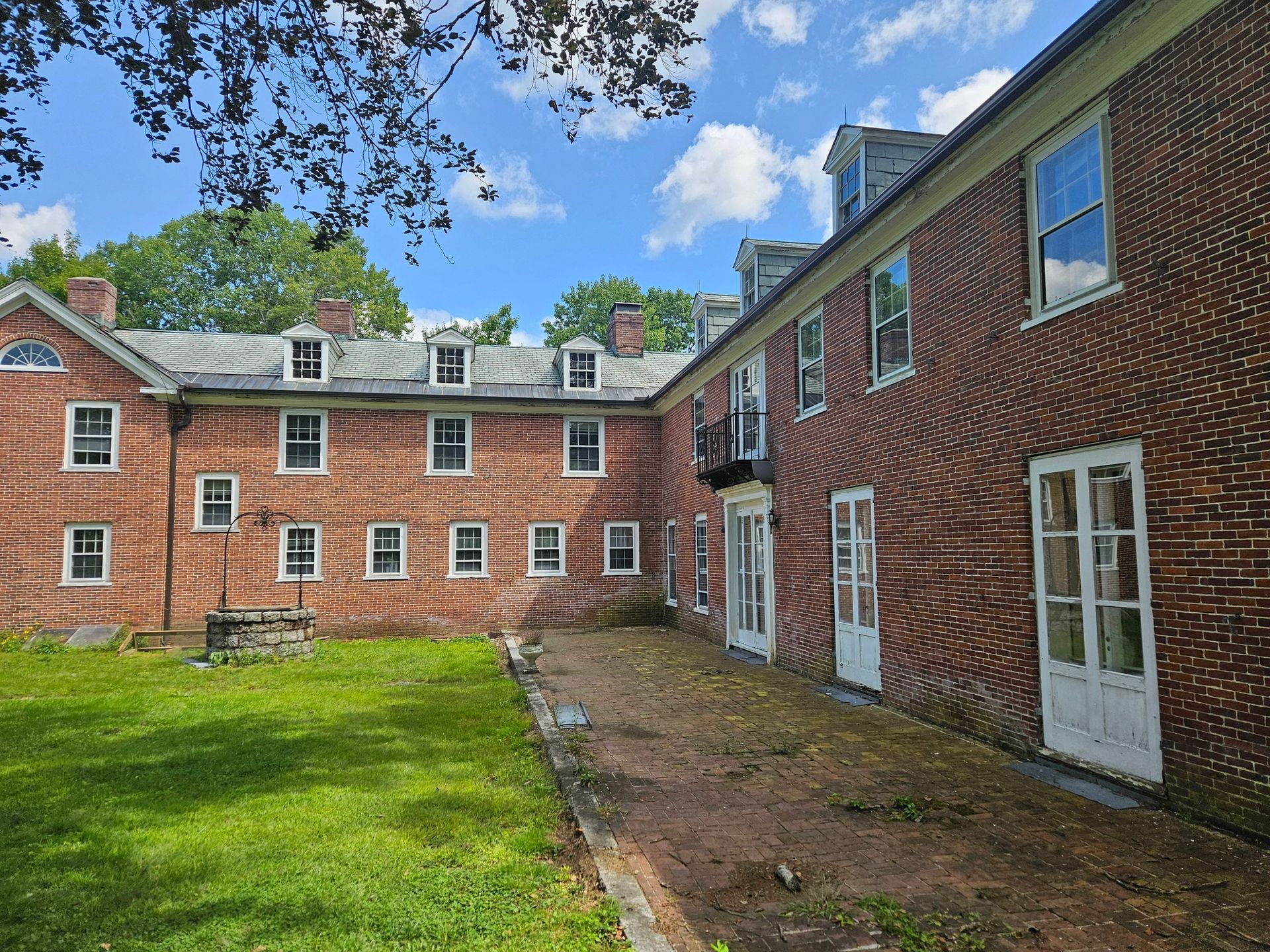 Red brick building with white-trimmed windows under a blue sky. A grassy yard and well are in the foreground.